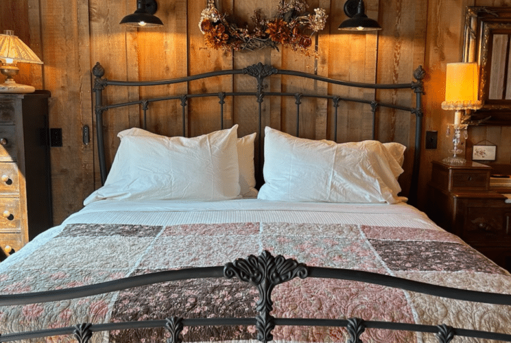 Image of King Bed against barnwood wall and beautiful quilt at foot of bed in The Granary Room accommodations at Inn at Sunset Mill Ranch in Wimberley Texas