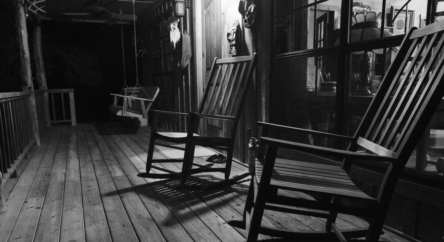 Large wooden front porch with wooden rocking chairs and swing at night