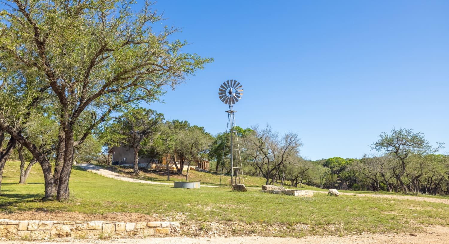 Large grassy area with green trees, windmill, property, and large green trees in the background