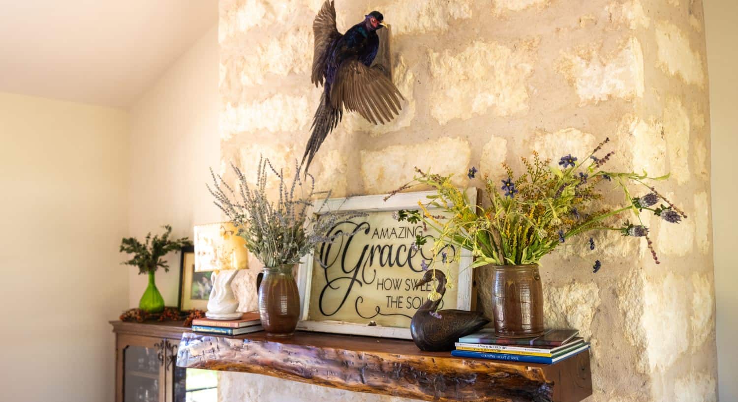Wooden mantel over a stone fireplace with vases of flowers, books, a lamp, and a sign which says Amazing Grace How Sweet the Sound