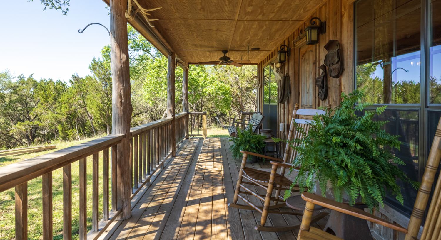 Exterioir view of the property's long wooden and covered front porch with wooden rocking chairs and views of large green trees