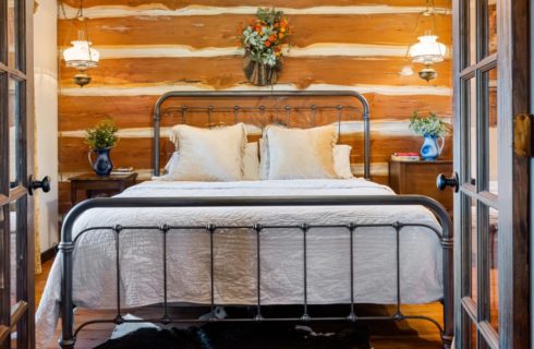 Bed with metal frame and white bedding with wood log paneling on the wall behind