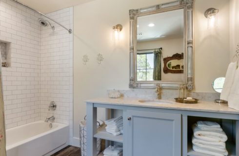 Bathroom with hardwood flooring, white bathtub and shower with white tile, large light blue vanity, and large framed mirror