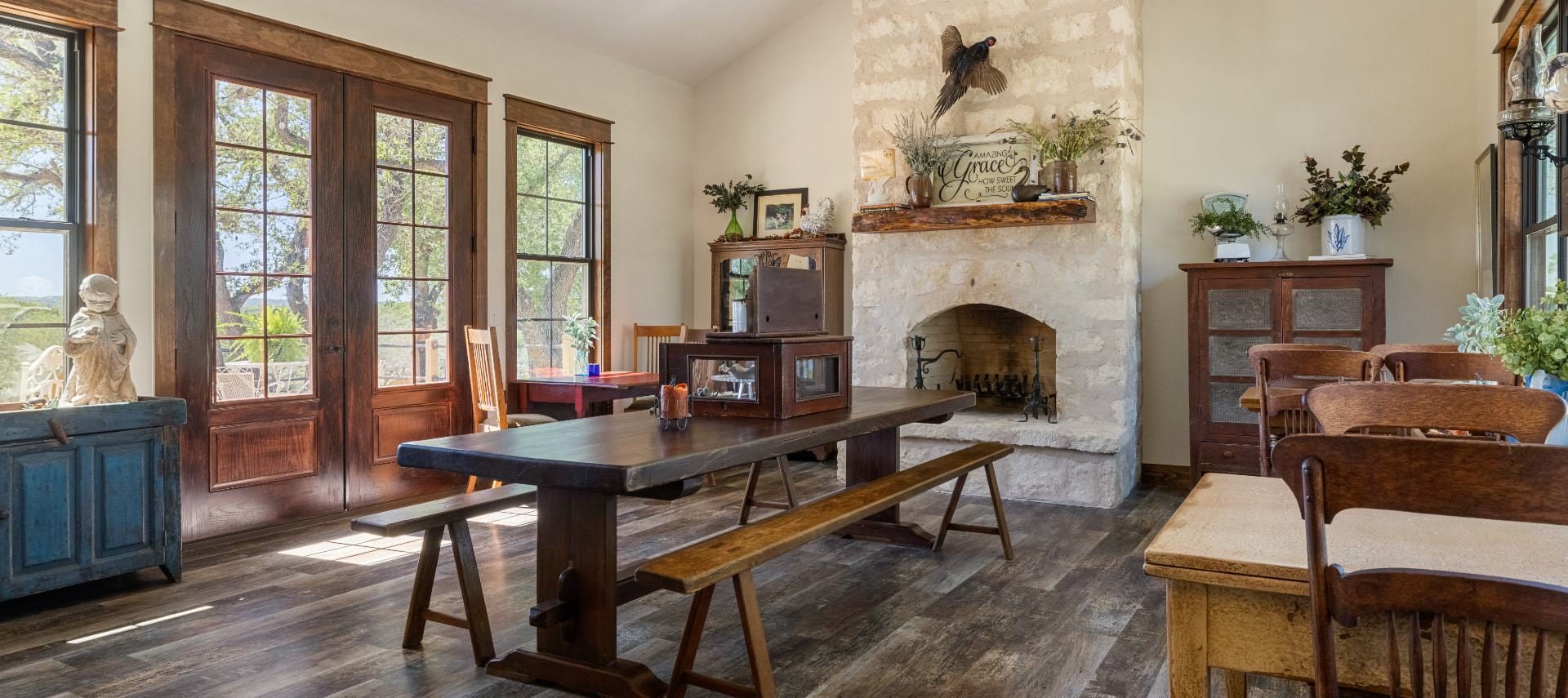 Large dining area with hardwood flooring, stone fireplace, dark wooden picnic table, small wooden tables and chairs, and views to the outside